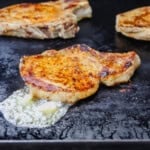 Three Blackstone pork chops cooking on the hot flat top with some melted garlic butter.