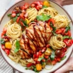 Two hands holding a large serving bowl of bruschetta chicken pasta.