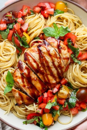 Two hands holding a large serving bowl of bruschetta chicken pasta.