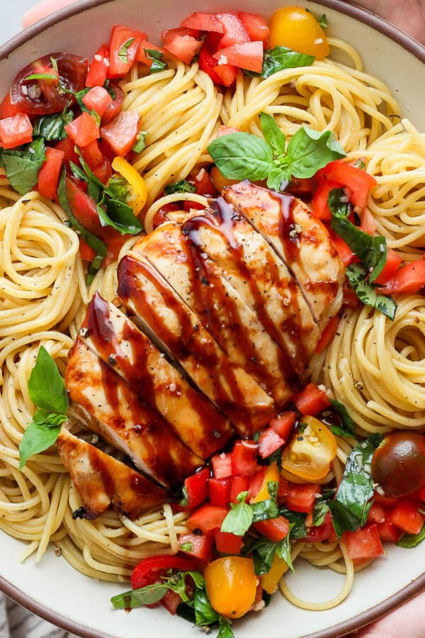 Two hands holding a large serving bowl of bruschetta chicken pasta.