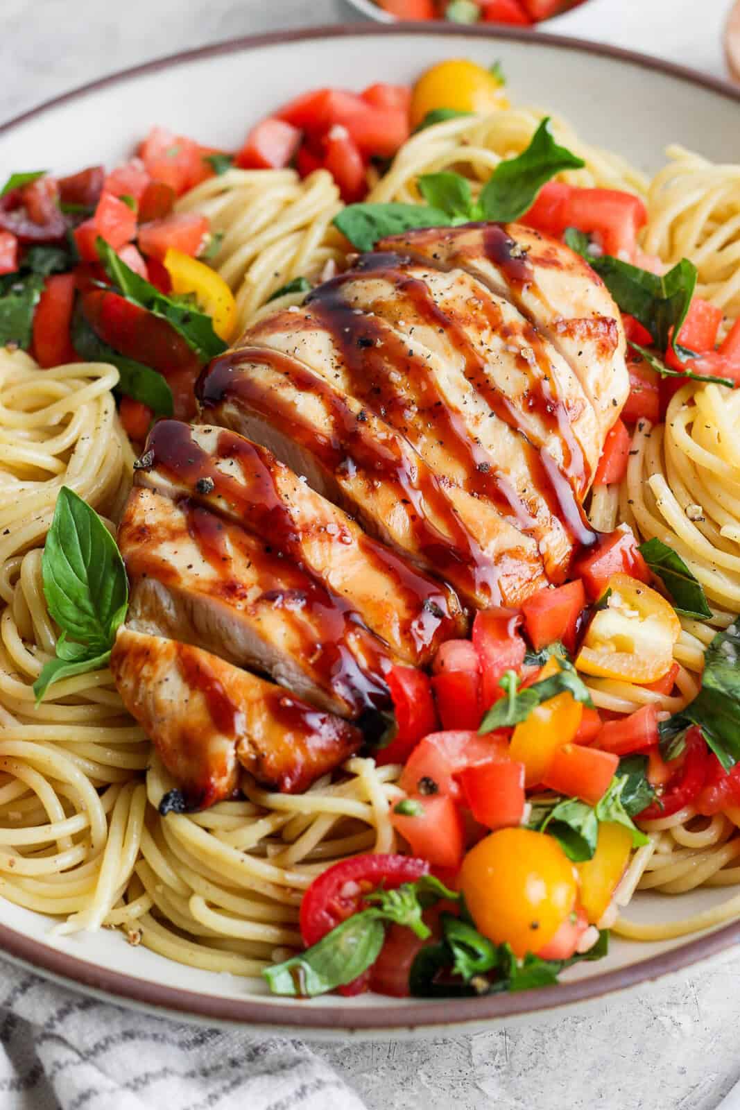Bruschetta chicken pasta in a large bowl with the chicken cut into slices and a drizzle of balsamic glaze on top.