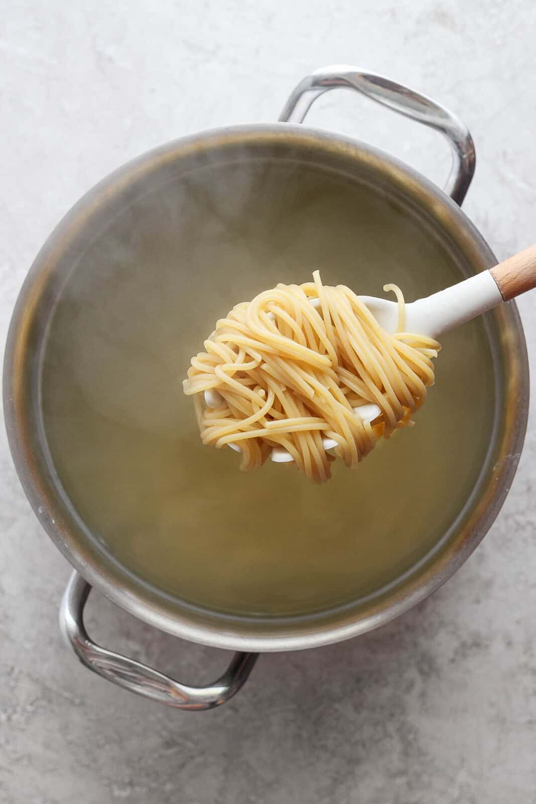 A spoon scooping cooked noodles out of a pot to make bruschetta chicken pasta.