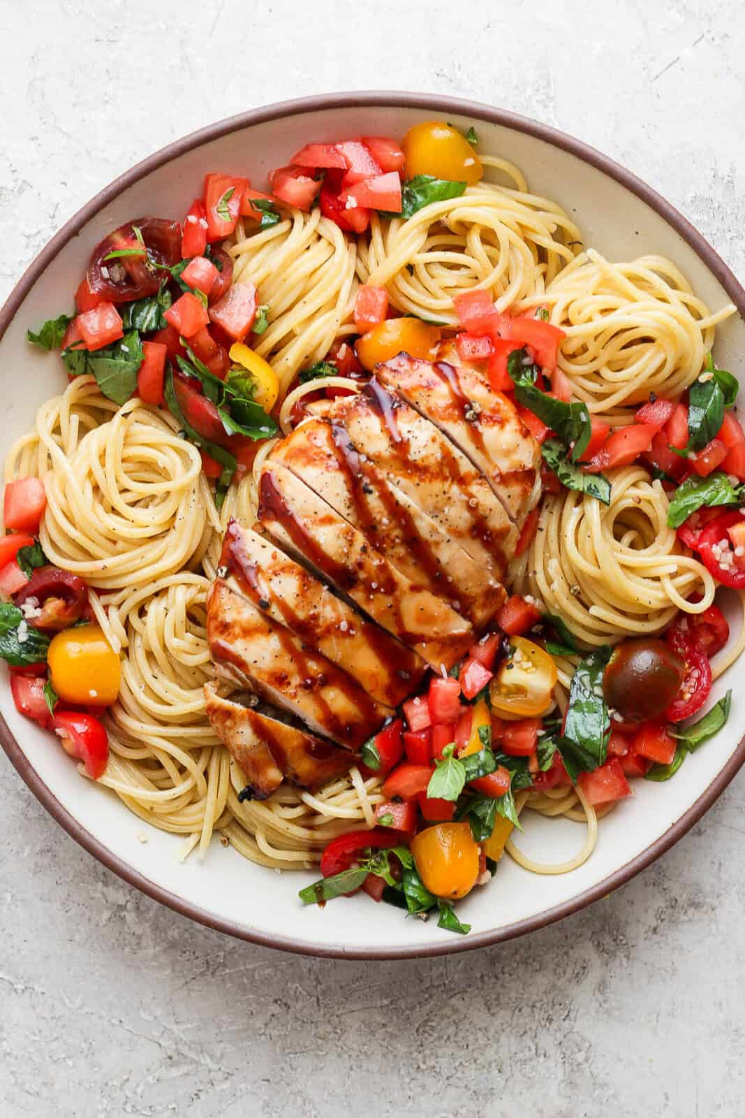 Bruschetta pasta in a large bowl with chicken on top and drizzled with balsamic glaze.