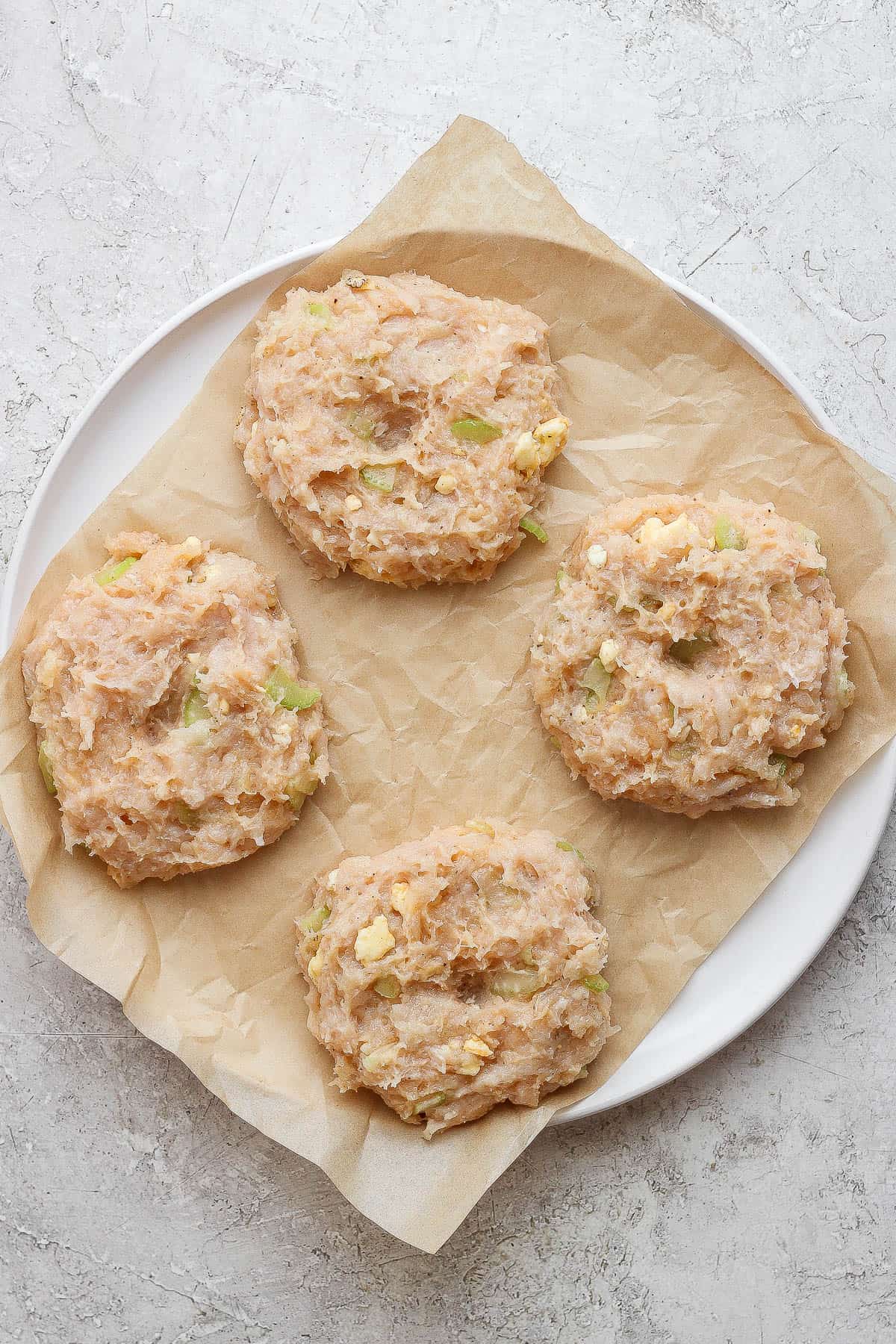 Buffalo Chicken Burgers - packed with flavor these burgers are a perfect weeknight dinner (and they make amazing leftovers!). GF + DF + Paleo + Whole30 #buffalochickenburger #buffalochicken #buffalochickenburgergrilled #buffalochickenburgerhealthy Buffalo chicken burgers on a piece of parchment paper before being cooked.