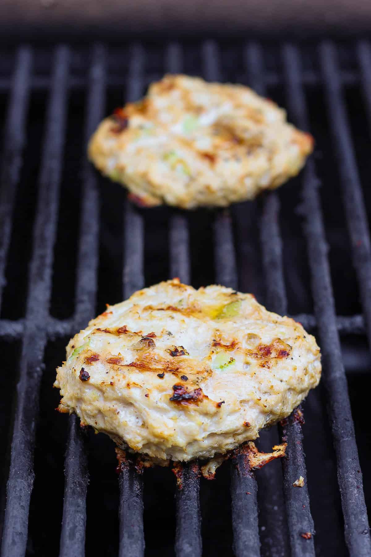 Buffalo Chicken Burgers - packed with flavor these burgers are a perfect weeknight dinner (and they make amazing leftovers!). GF + DF + Paleo + Whole30 #buffalochickenburger #buffalochicken #buffalochickenburgergrilled #buffalochickenburgerhealthy Two buffalo chicken burgers cooking on the grill.