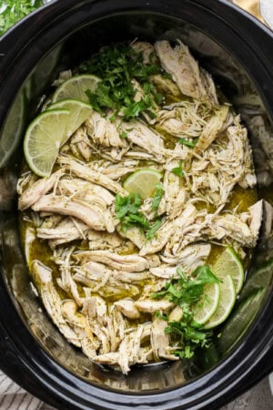 Crockpot cilantro lime chicken with fresh cilantro and lime wedges in the crockpot.