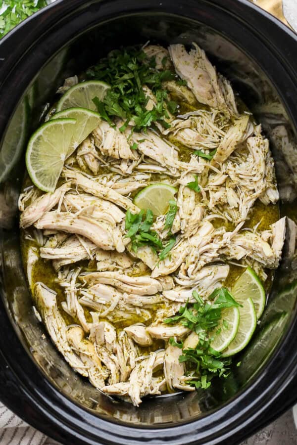 Crockpot cilantro lime chicken with fresh cilantro and lime wedges in the crockpot.