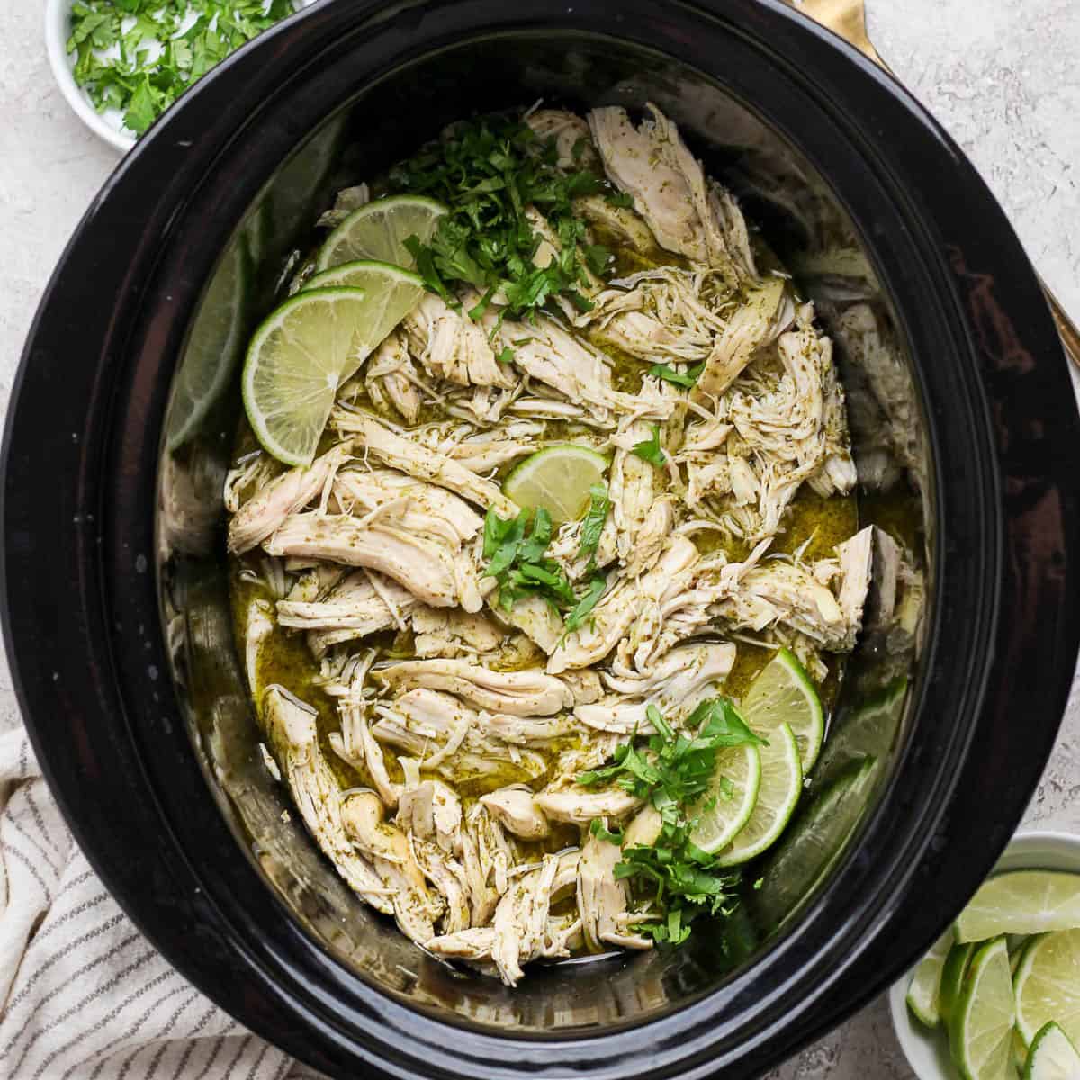 Crockpot cilantro lime chicken with fresh cilantro and lime wedges in the crockpot.