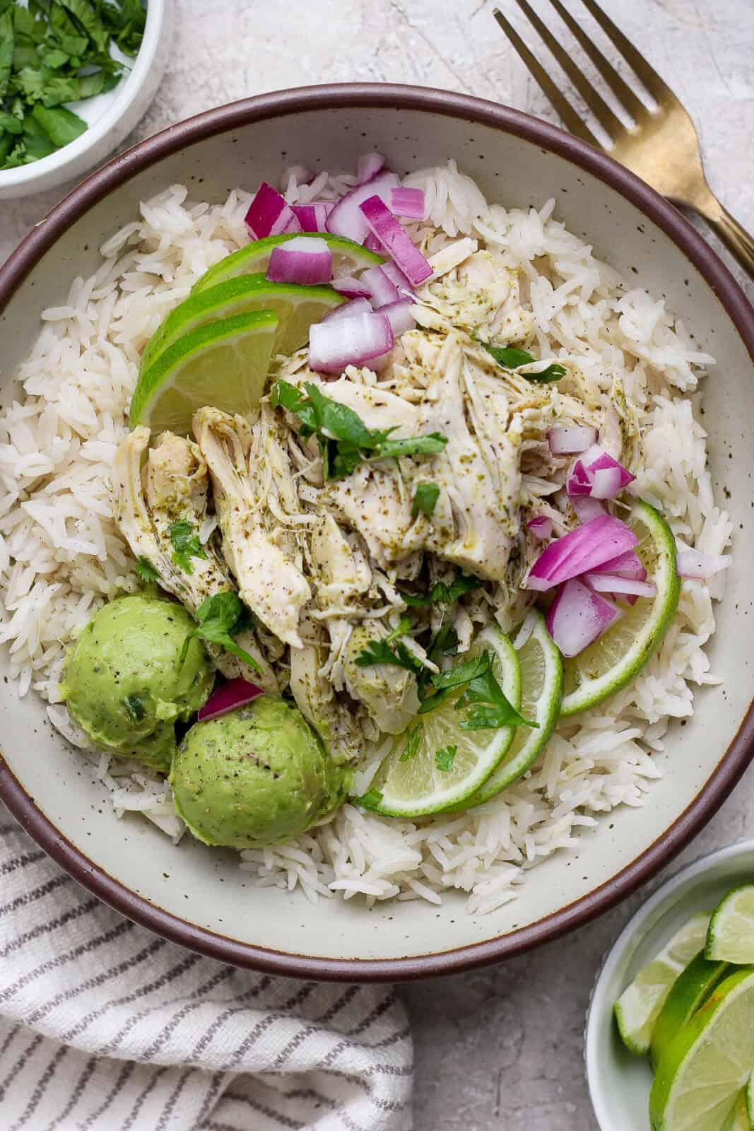 Crockpot cilantro lime chicken served on rice with guacamole and lime slices.