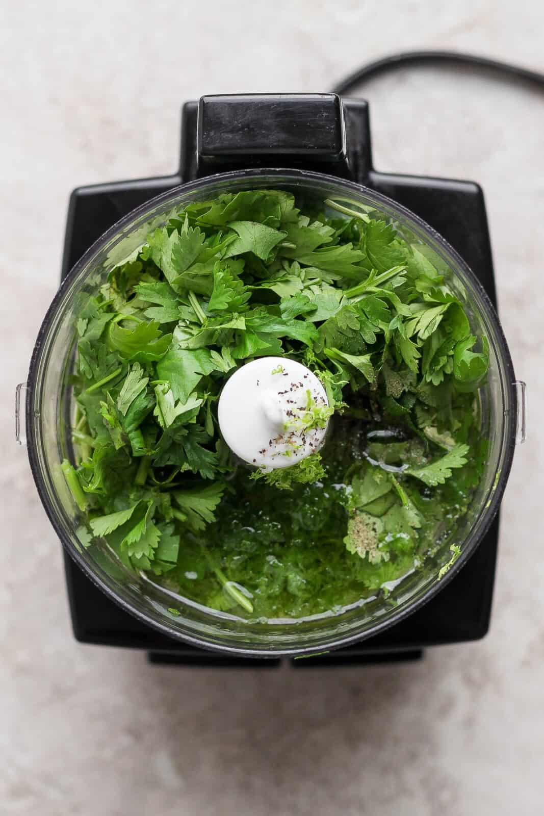 Cilantro, oil, lime juice, lime zest, garlic, salt and pepper in a food processor before blending to make crockpot cilantro lime chicken.
