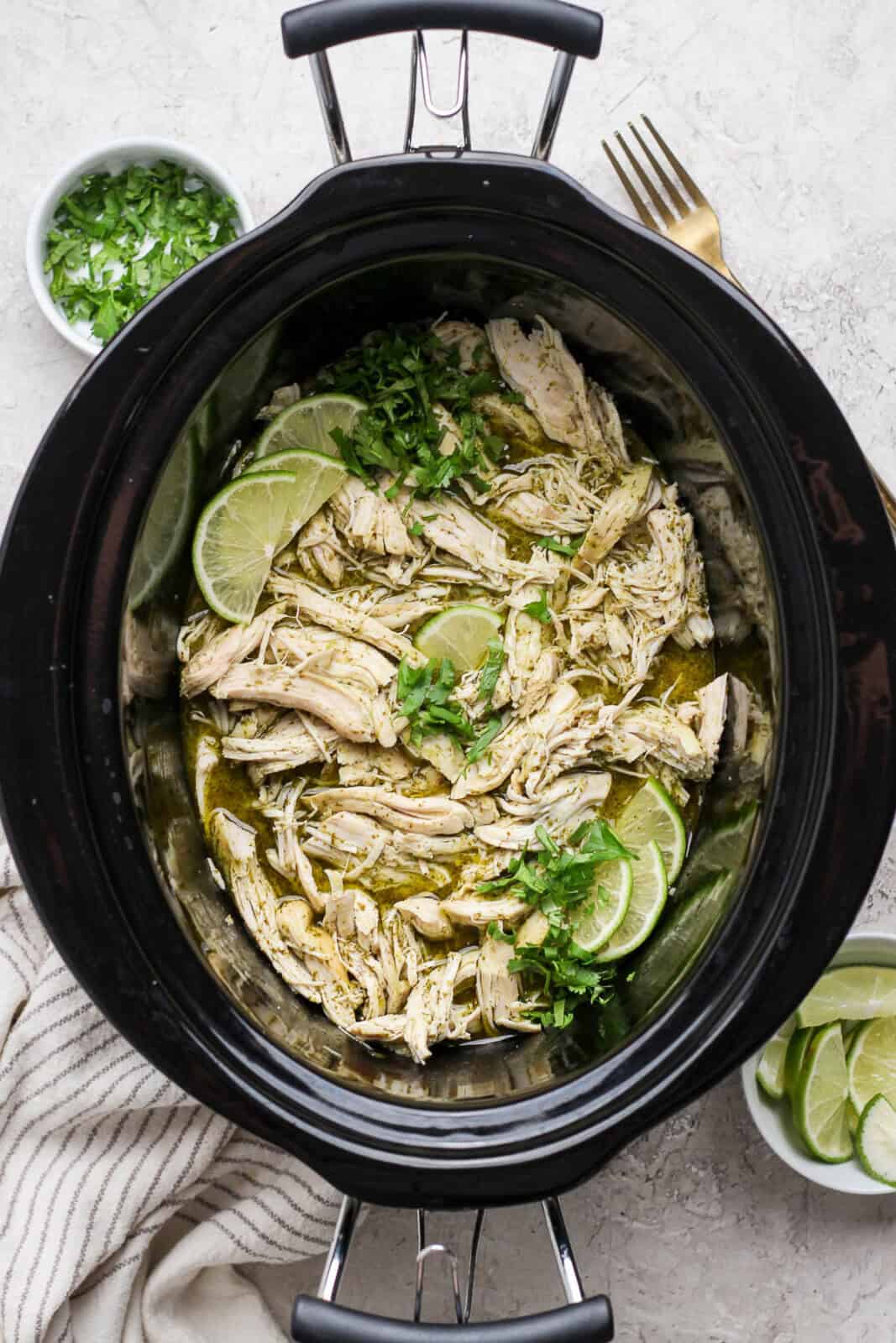 Crockpot cilantro lime chicken in the slow cooker with fresh cilantro and lime slices.
