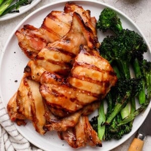 Grilled boneless chicken thighs on a white plate with grilled broccolini.