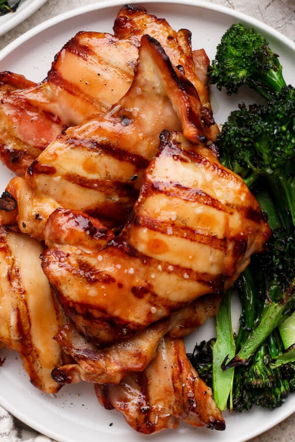 Grilled boneless chicken thighs on a white plate with grilled broccolini.