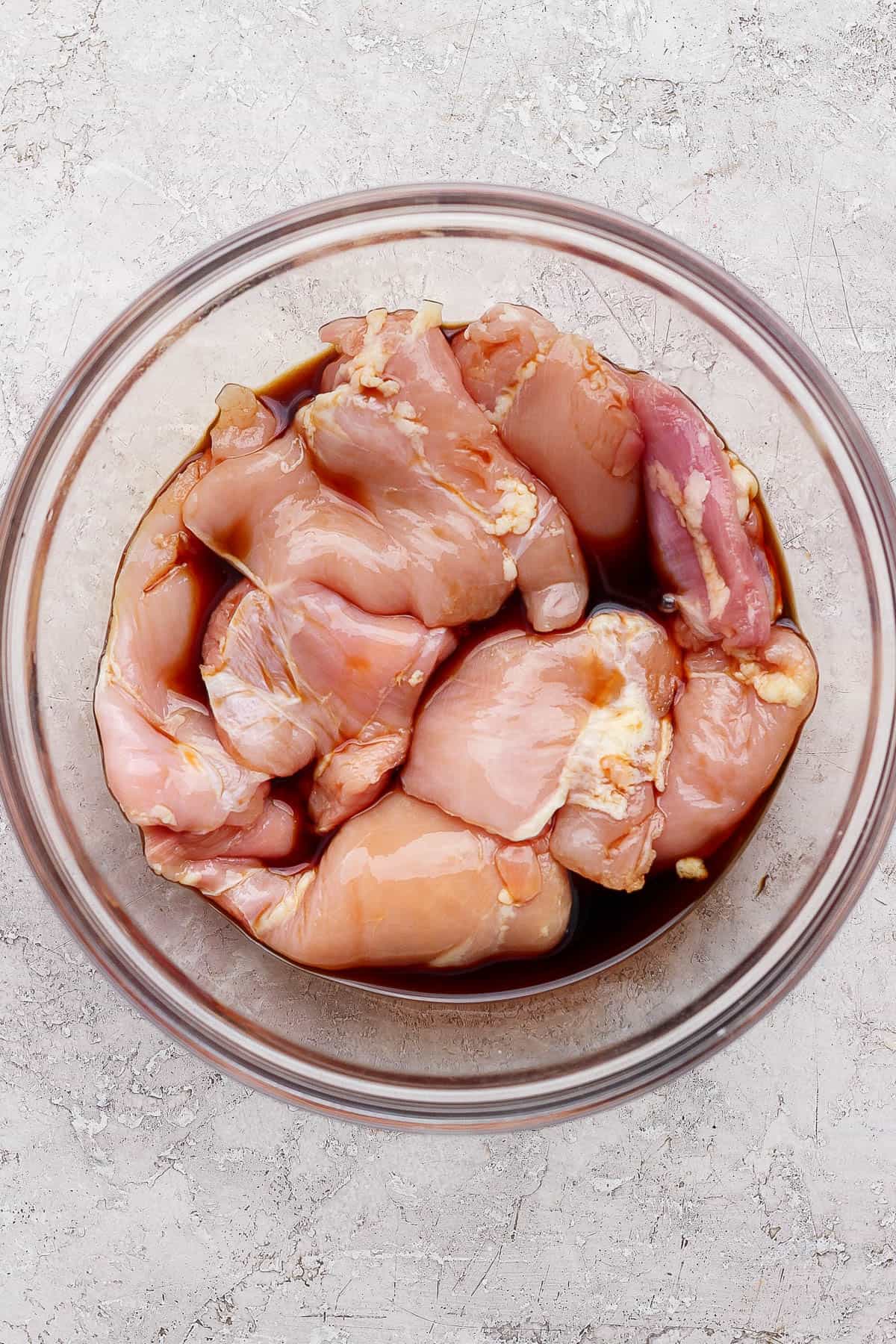 Boneless skinless chicken thighs in a glass bowl with soy sauce before grilling.