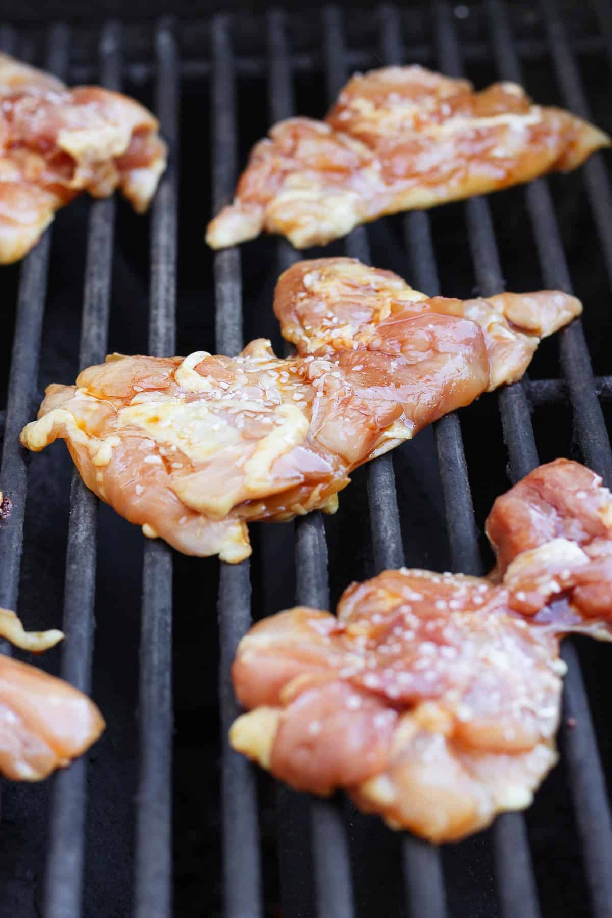 Boneless skinless chicken thighs on a grill before flipping.