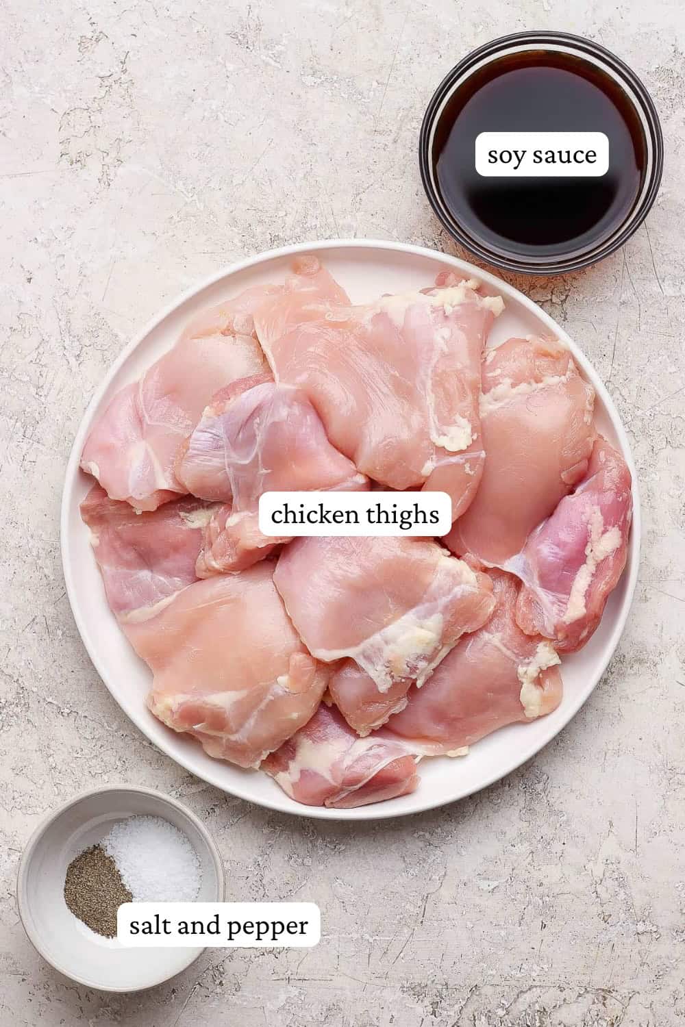 Raw chicken thighs on a plate next to a bowl of soy sauce and a small bowl of salt and pepper to make grilled chicken thighs.