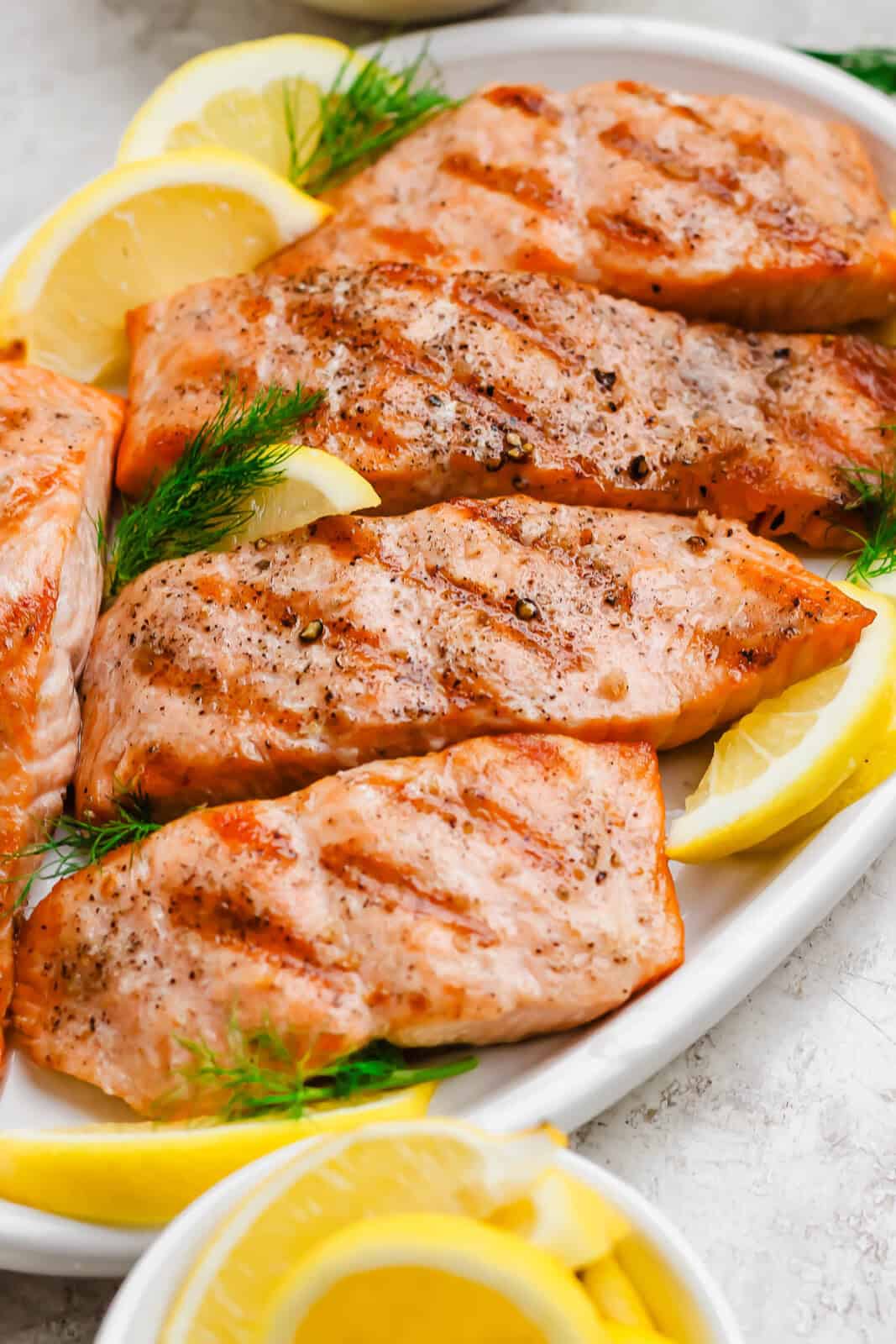 Grilled salmon fillets on a large white platter with lemon wedges.