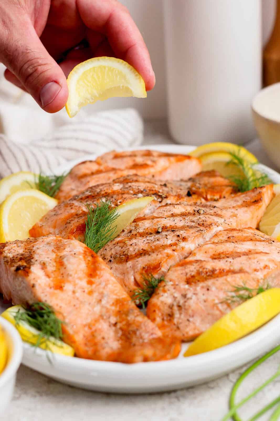 A lime wedge squeezed over several grilled salmon fillets on a platter.