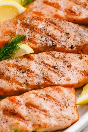 Several grilled salmon fillets on a platter with lemon wedges.