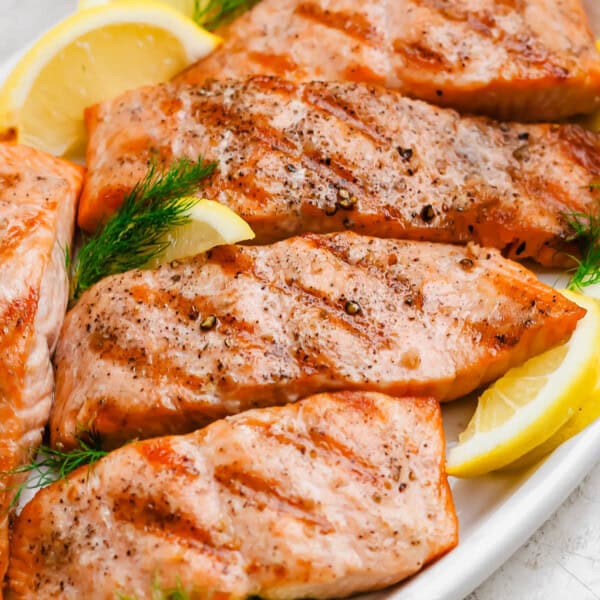 Several grilled salmon fillets on a platter with lemon wedges.