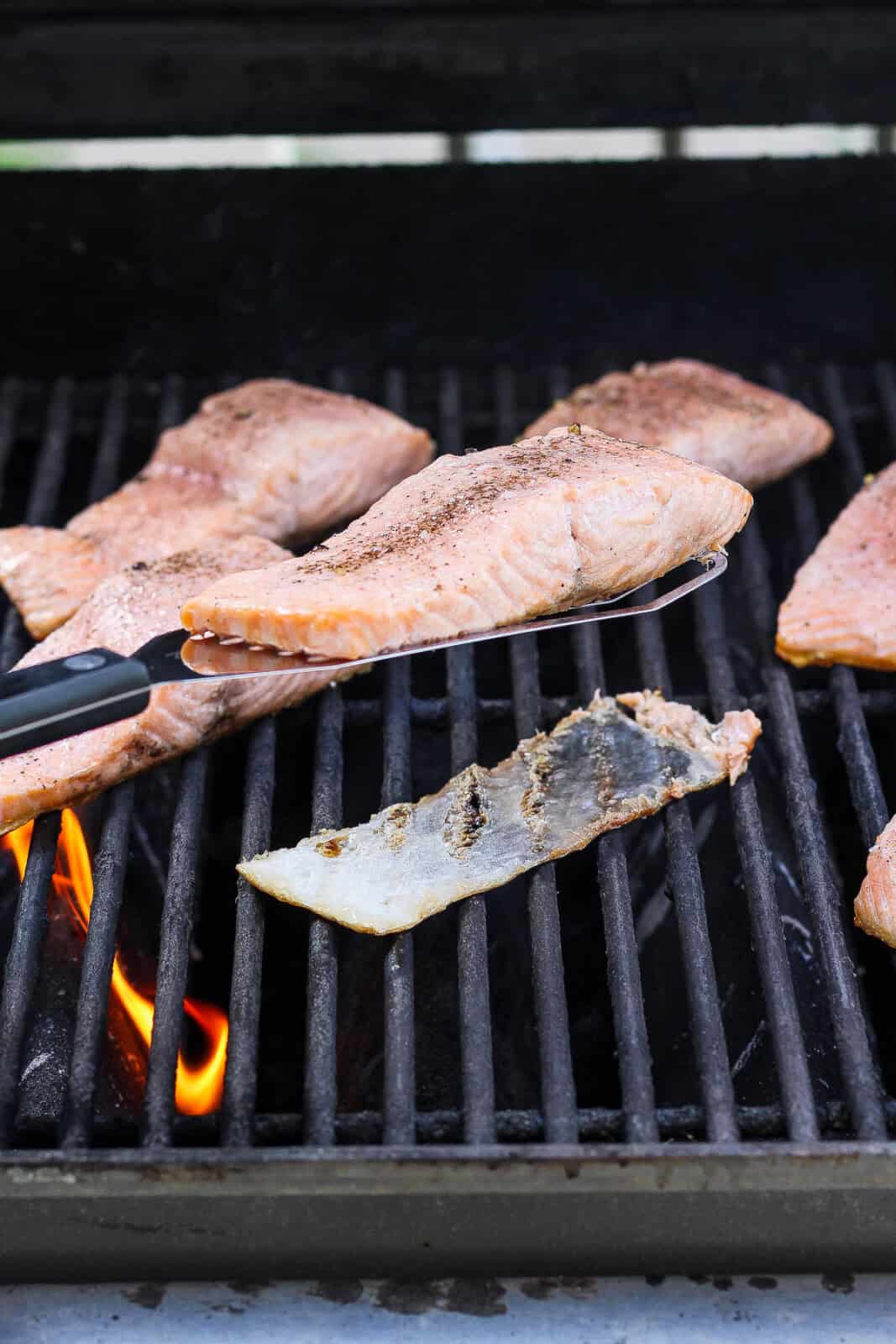 A spatula lifting one salmon fillet up while making grilled salmon.