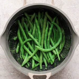 Steamed green beans in a pot with a steamer basket.
