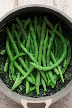 Steamed green beans in a pot with a steamer basket.