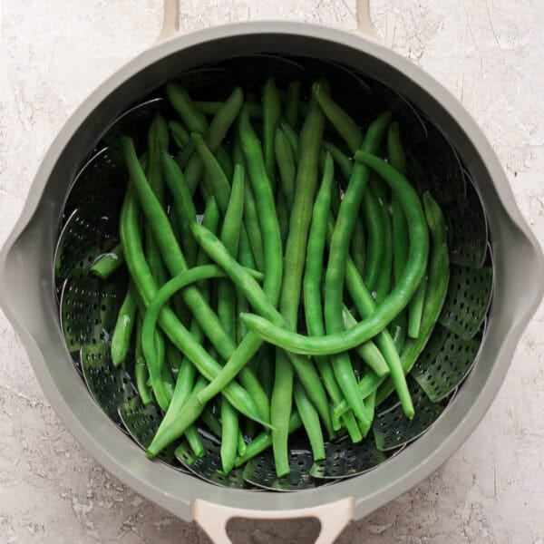 Steamed green beans in a pot with a steamer basket.