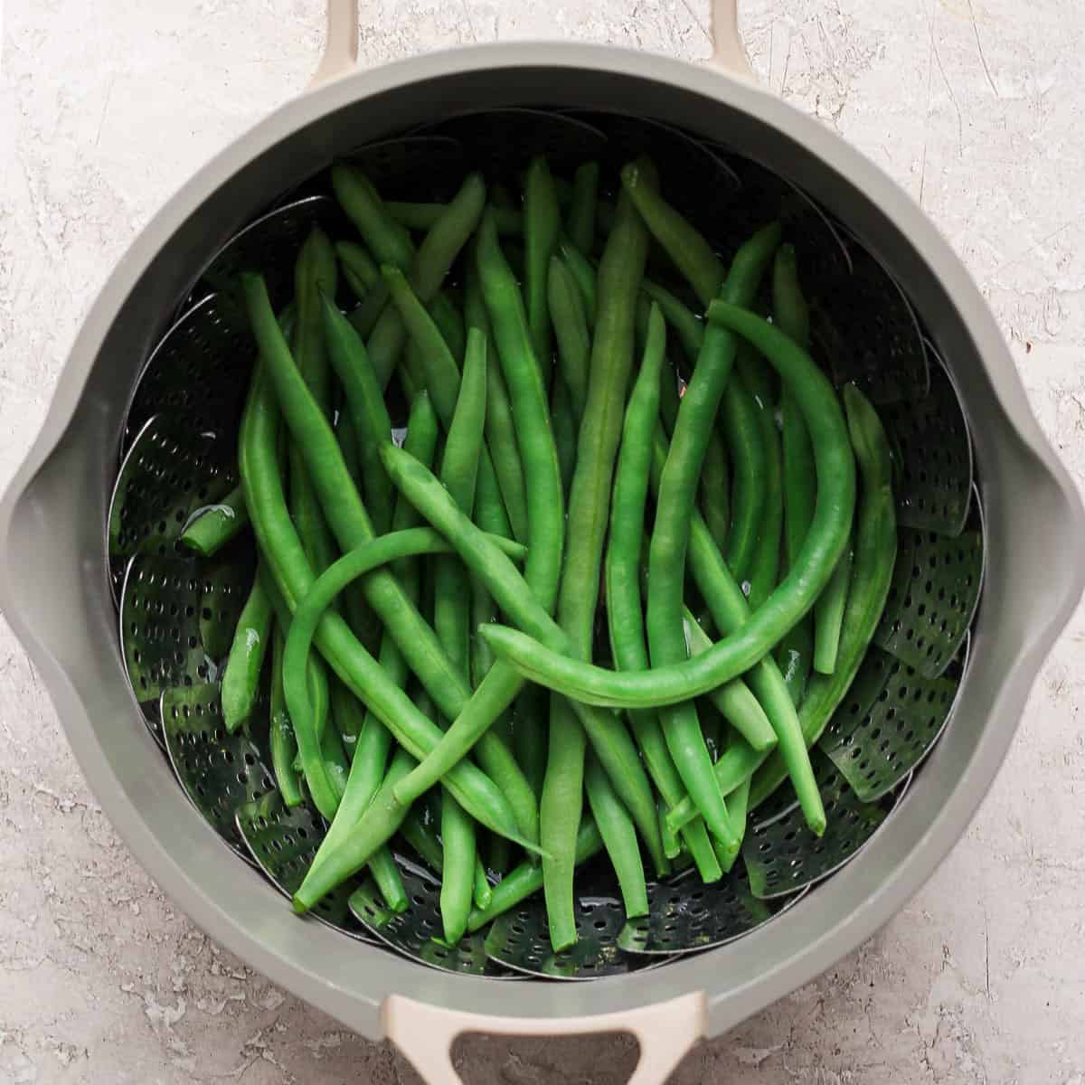 Steamed green beans in a pot with a steamer basket.