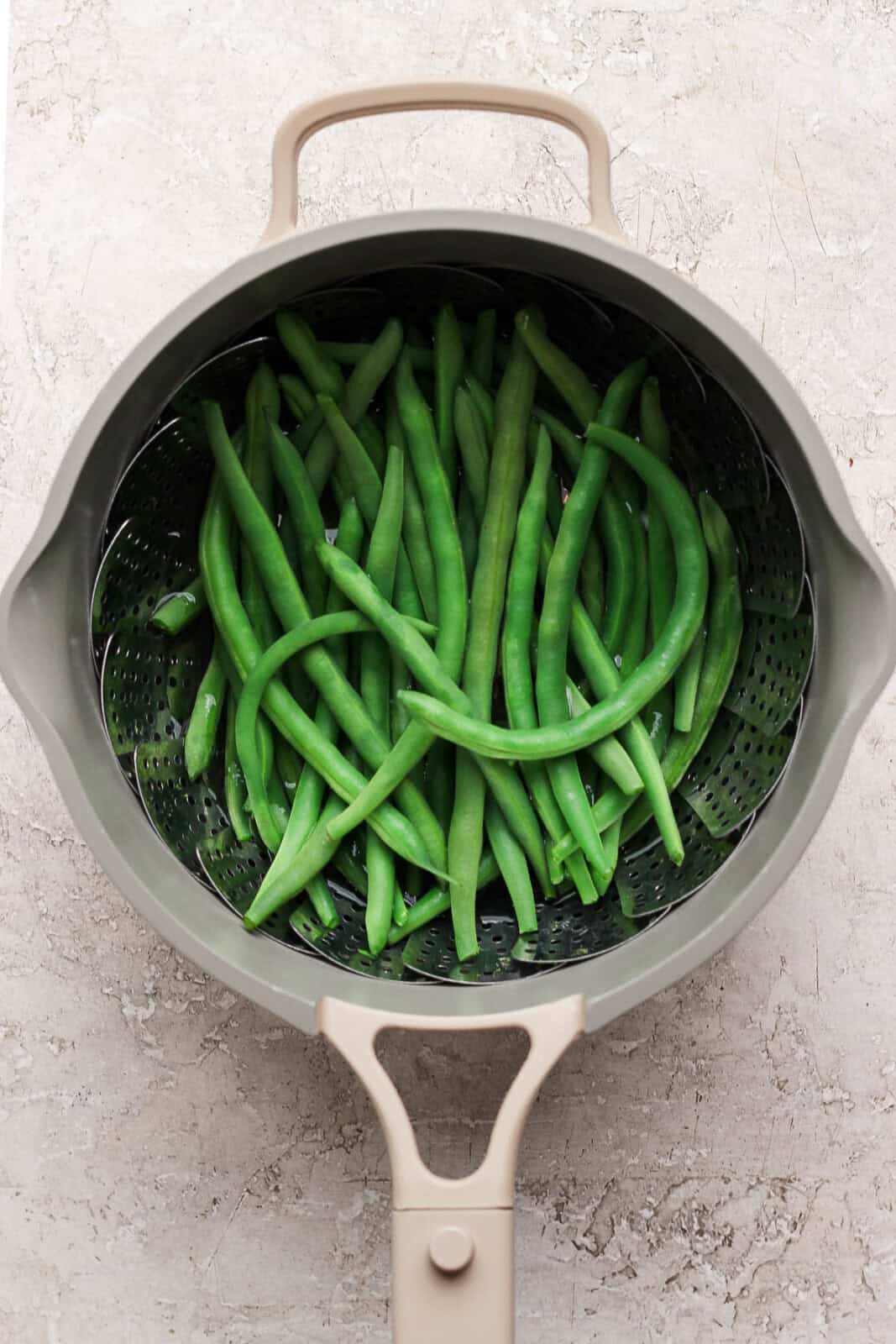 Steamed green beans in a saucepan with a steamer basket.