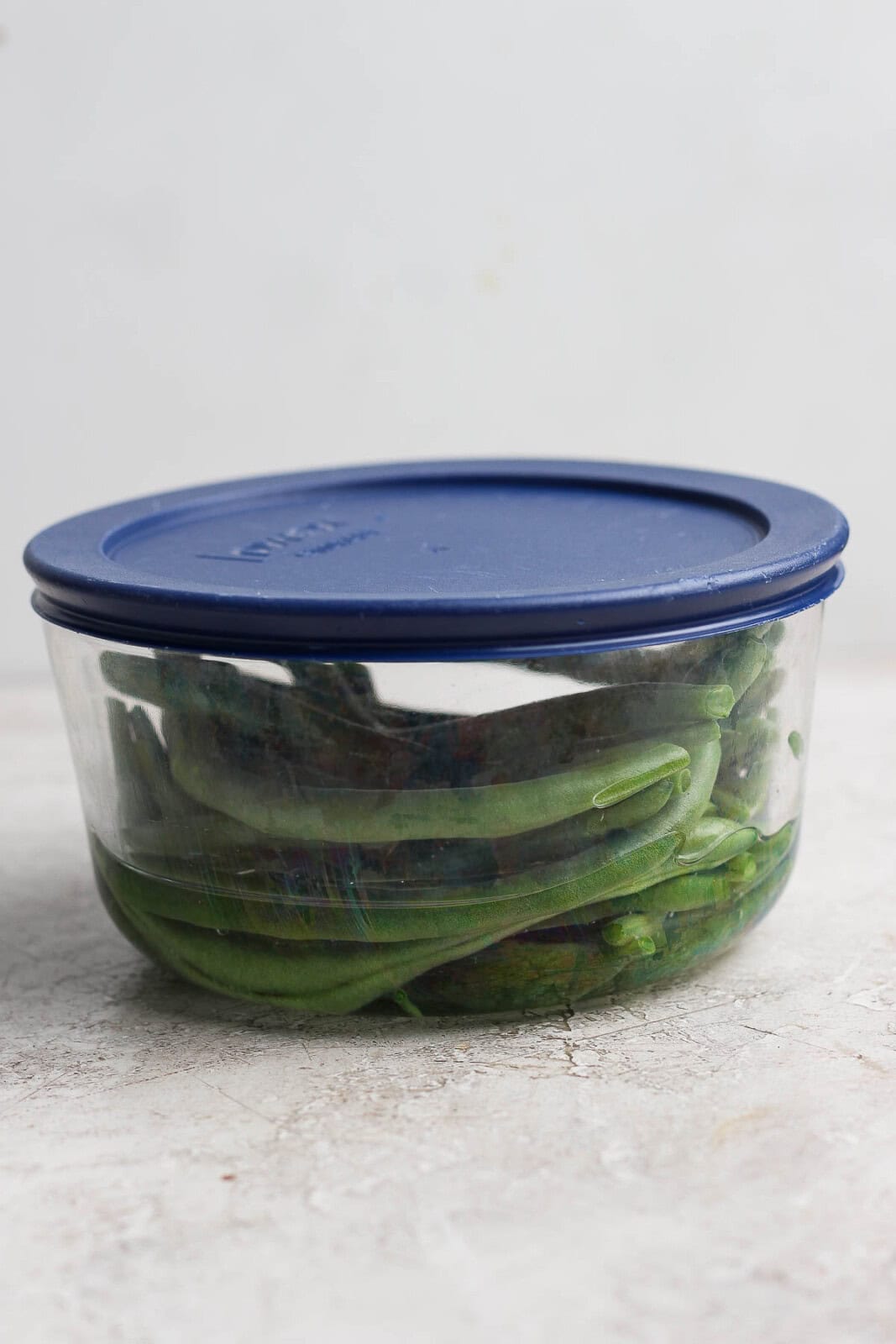 Steamed green beans in a microwave safe container with water and a lid on top.