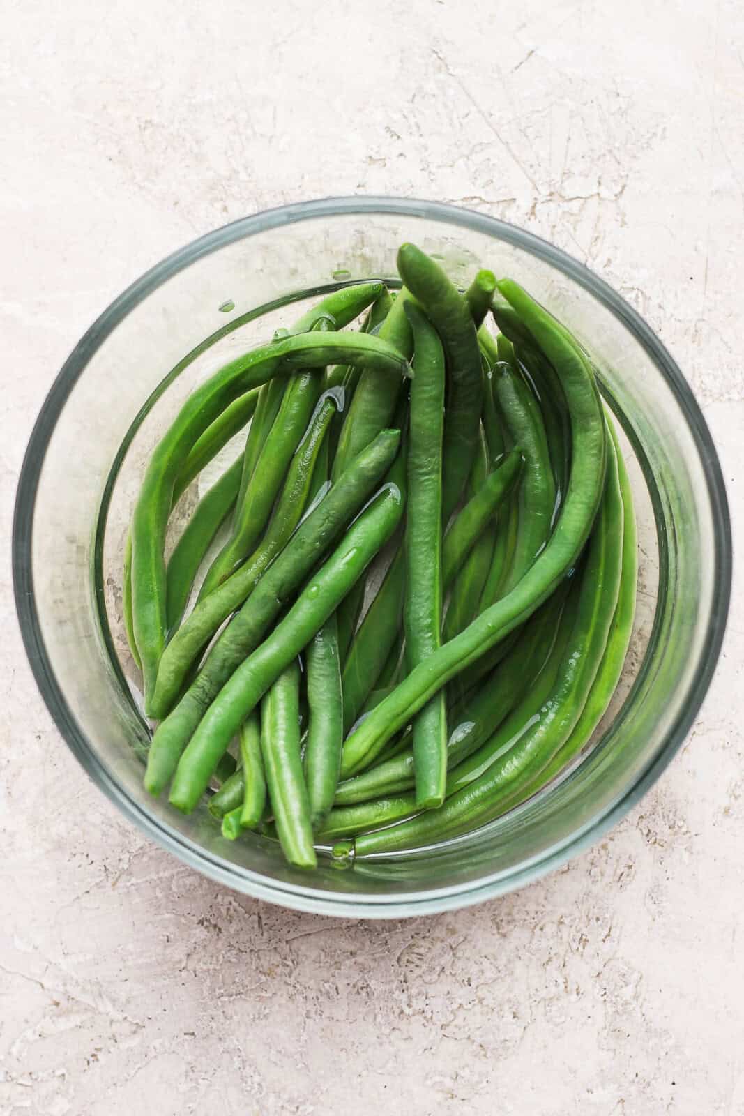 Microwave steamed green beans in a glass bowl with a bit of water in the bottom.