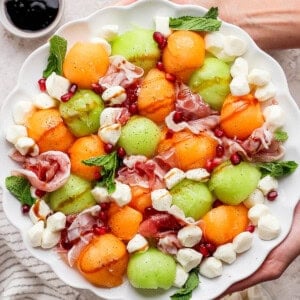 Two hands holding a platter of caprese melon salad.