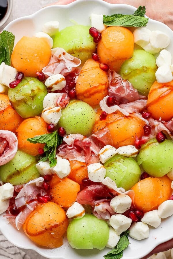 Two hands holding a platter of caprese melon salad.