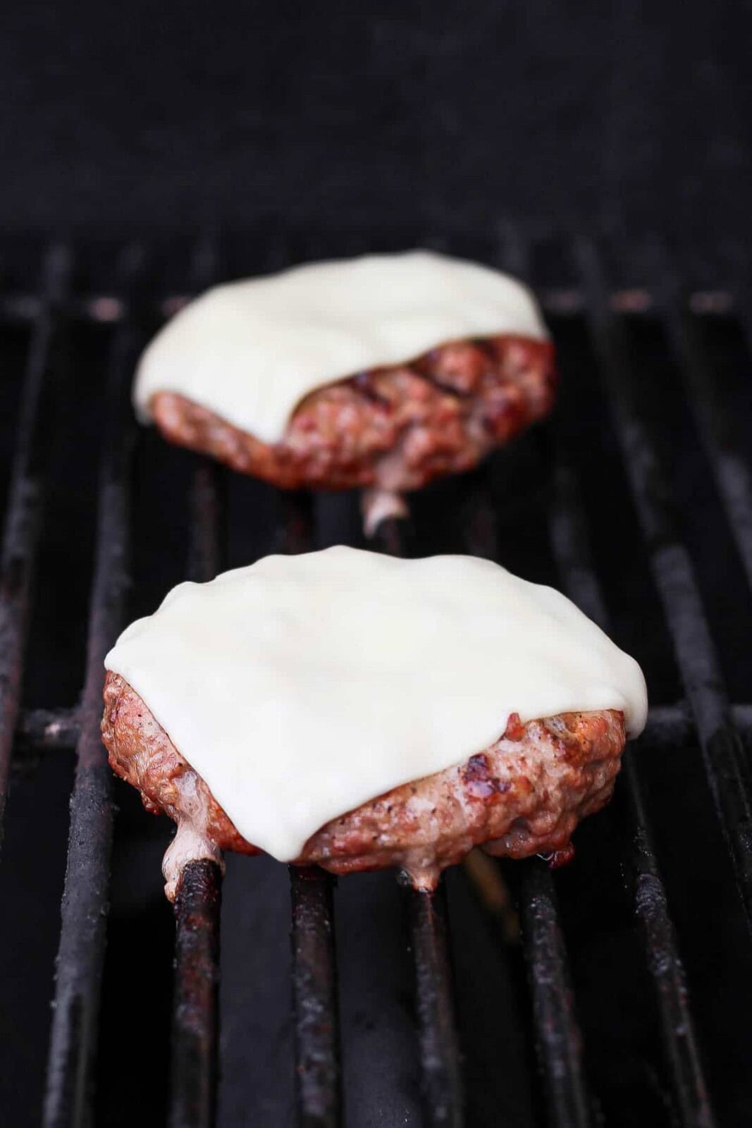 Pork burger patties with cheese cooking on the grill.