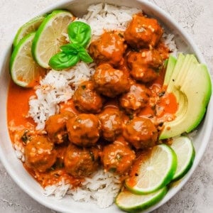 Red curry meatballs over rice with lime slices and avocado.