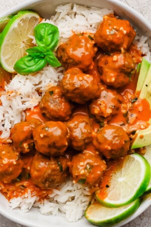 Red curry meatballs over rice with lime slices and avocado.