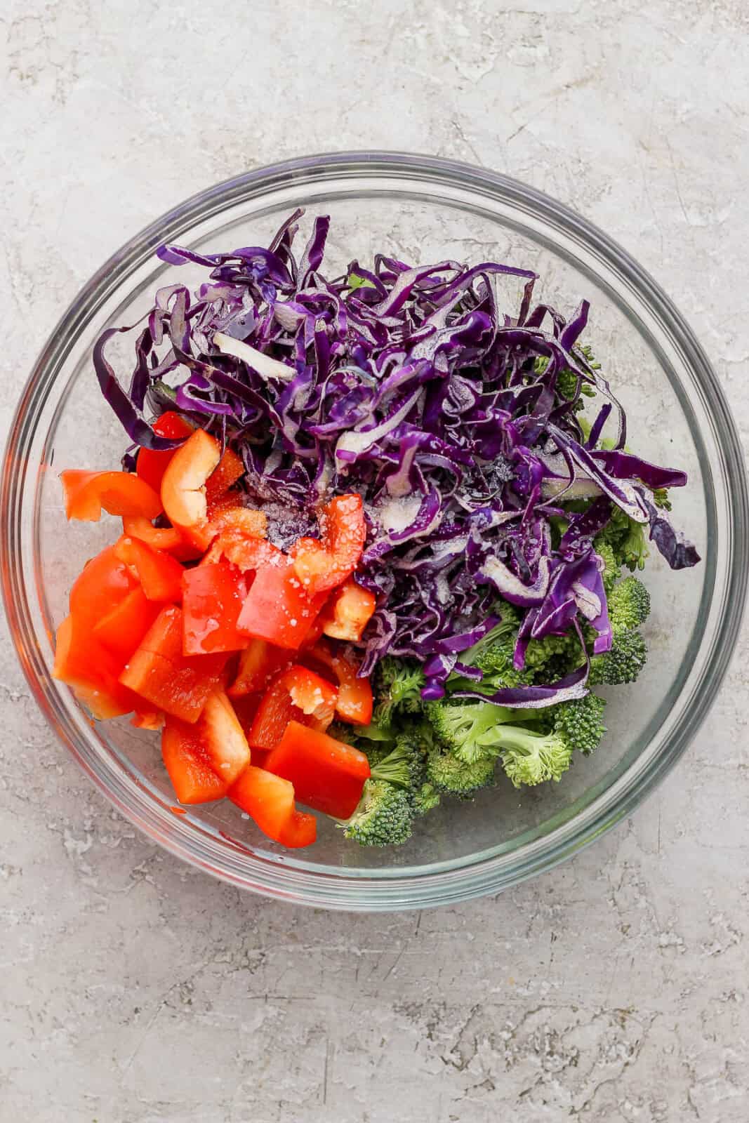 Purple cabbage, broccoli, and red pepper in a glass bowl before cooking for a salmon power bowl.