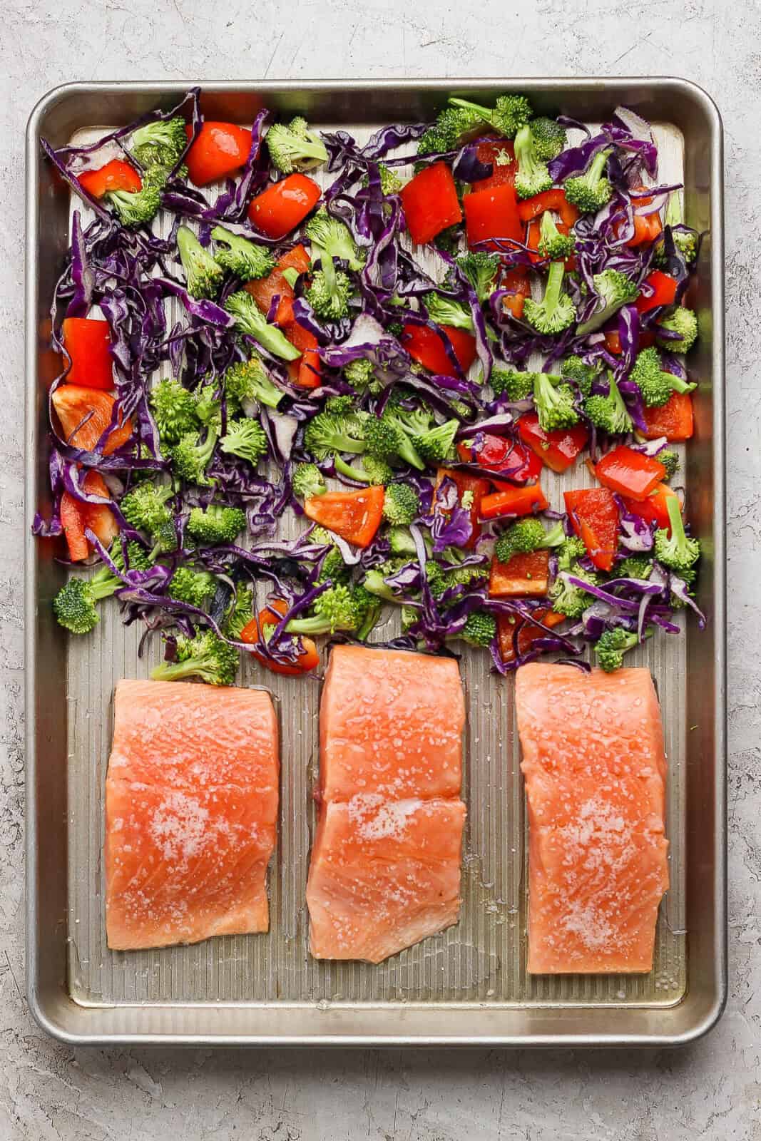 Fresh veggies added to the sheet pan with salmon before baking for a salmon power bowl.