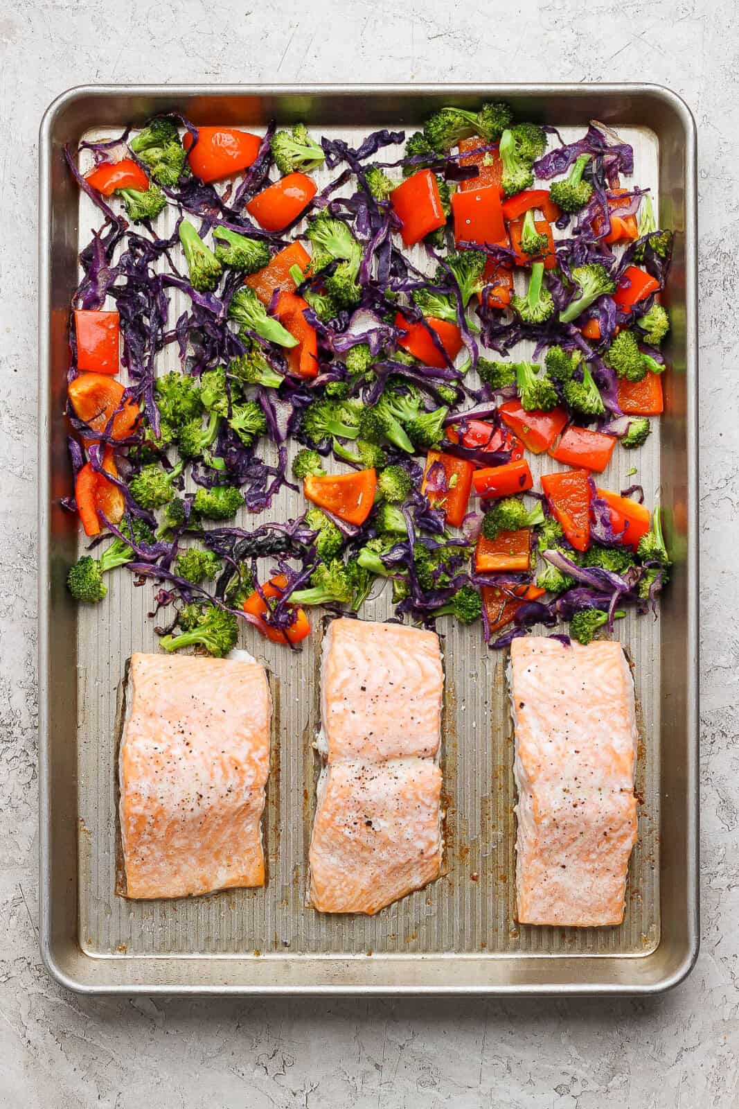 Cooked salmon and vegetables on a sheet pan for a salmon power bowl.