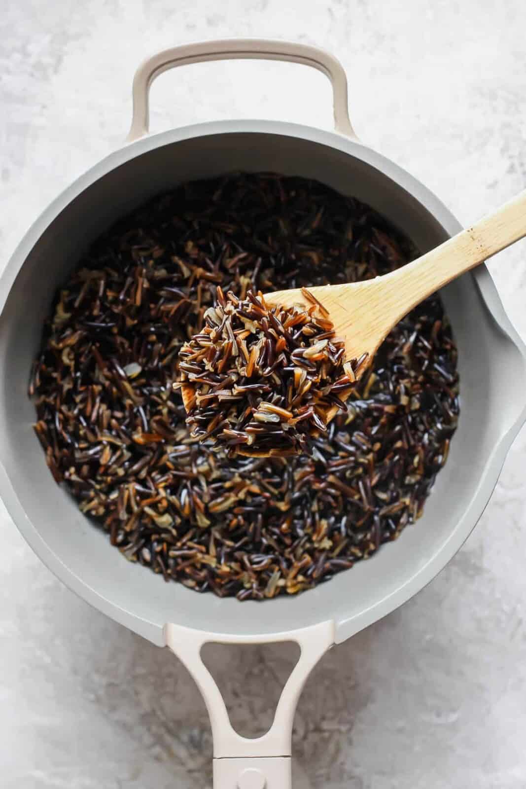 A wooden spoon scooping some cooked wild rice out of a pot to serve in a salmon power bowl.