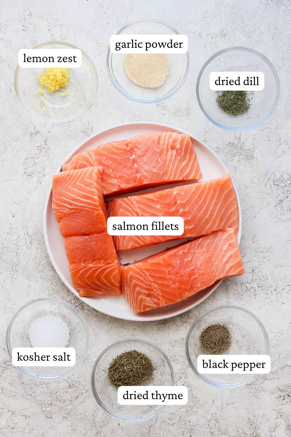 Salmon fillets on a plate surrounded by small bowls of salmon seasoning ingredients with labels.