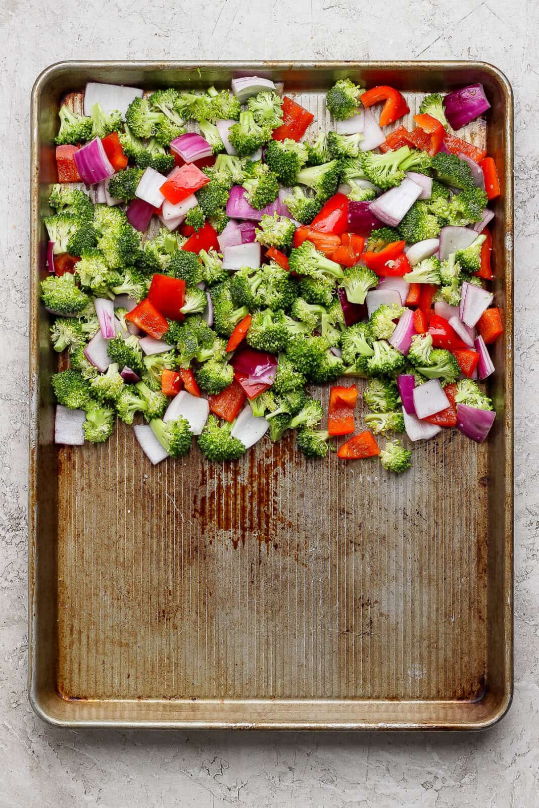 Broccoli, bell pepper, and red onion tossed with oil, salt and pepper on one side of a sheet pan before baking.
