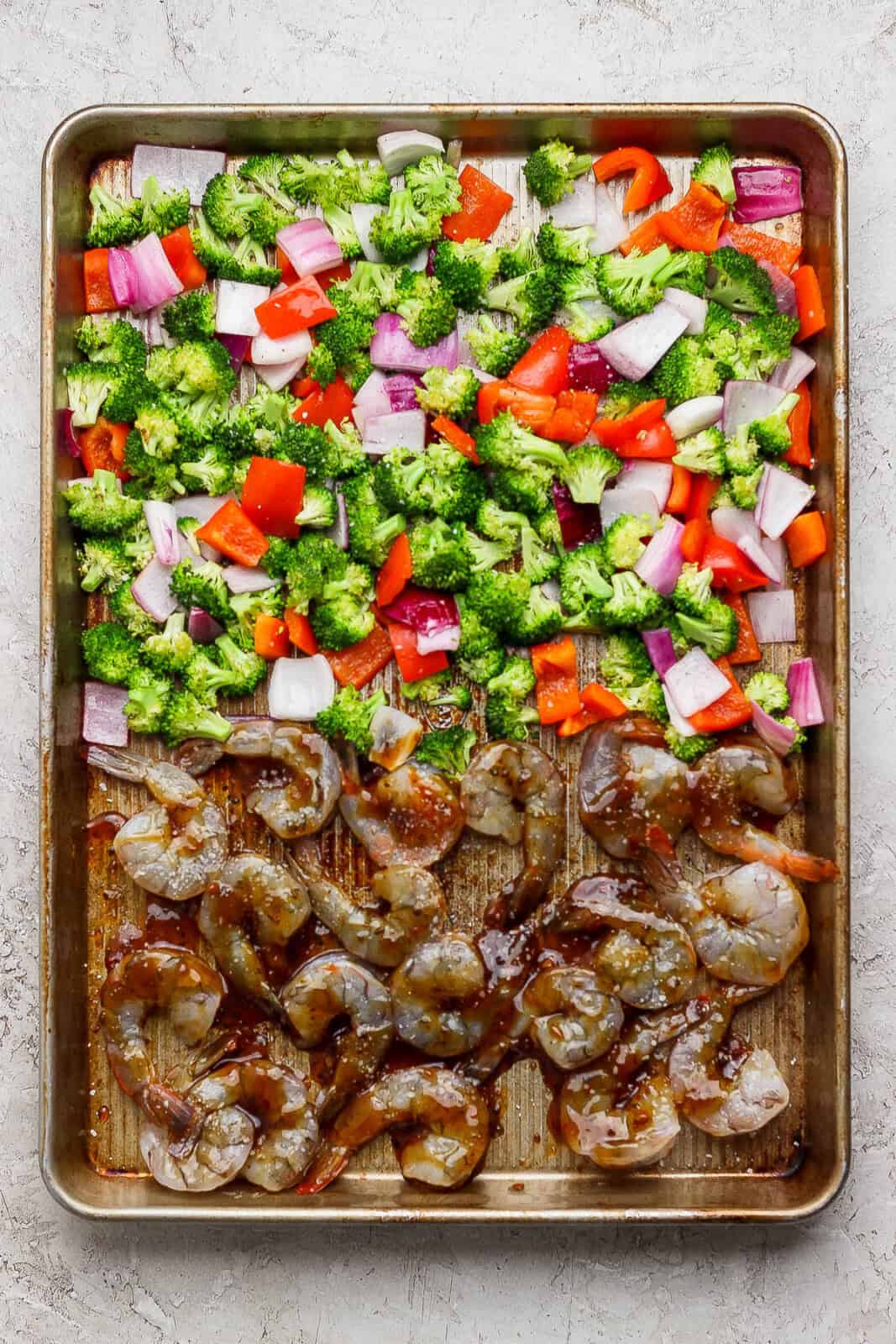 Roasted vegetables on one side of a sheet pan and raw shrimp tossed in teriyaki sauce on the other side of the pan to make a shrimp sheet pan dinner.
