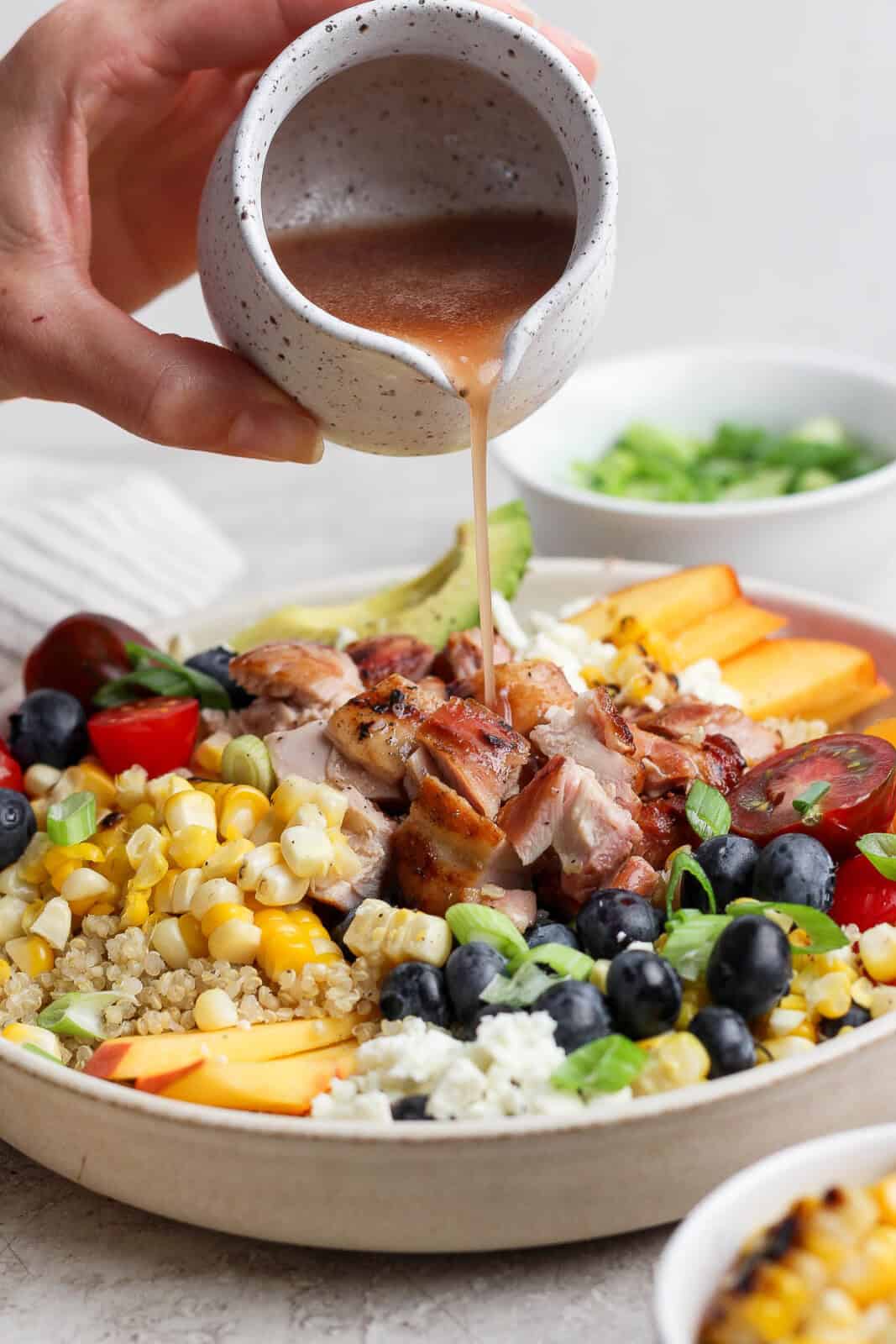 Balsamic vinaigrette being poured on a summer quinoa salad bowl.