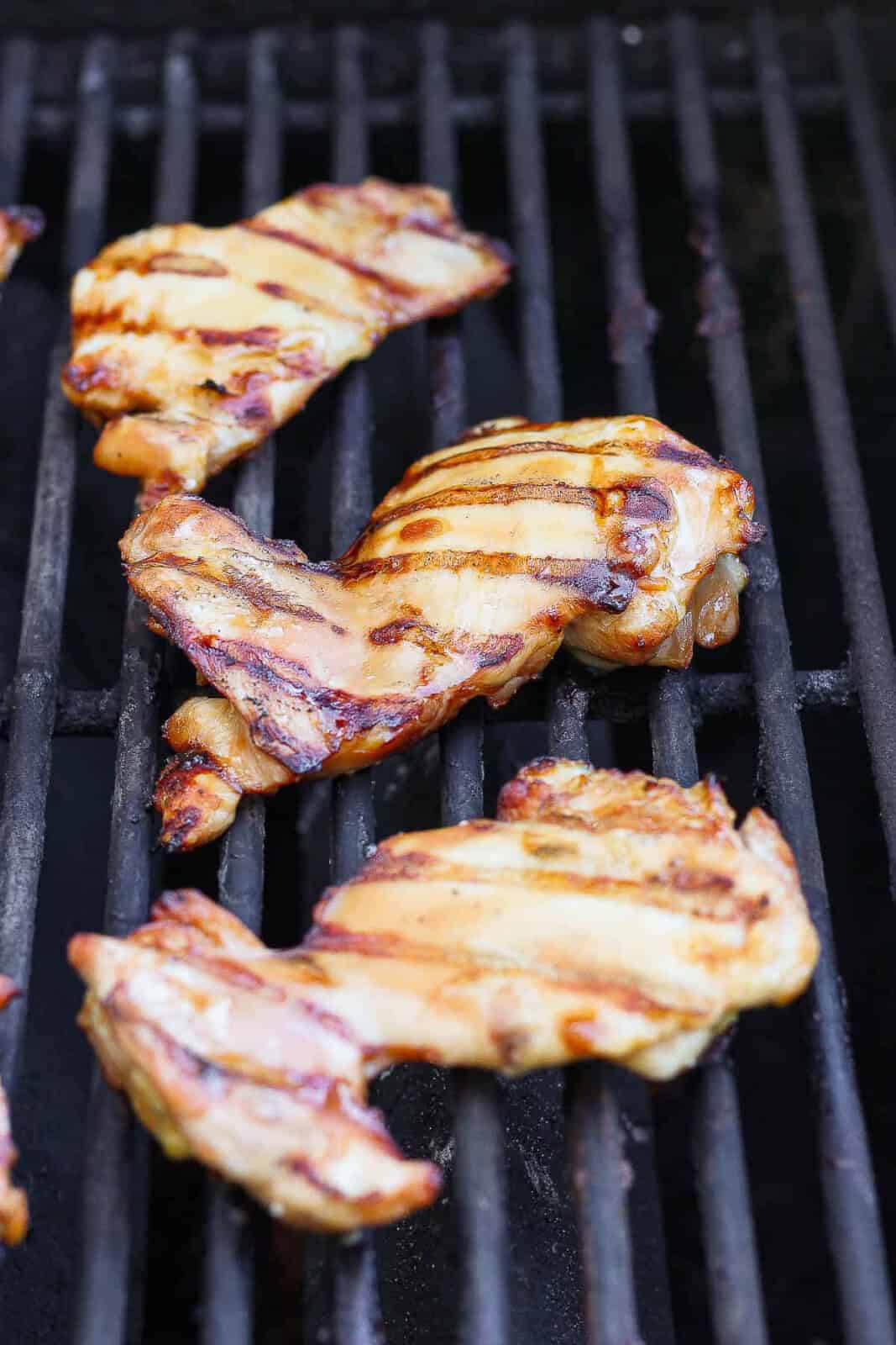 Grilled chicken thighs on the grill before being added to summer quinoa salad bowls.