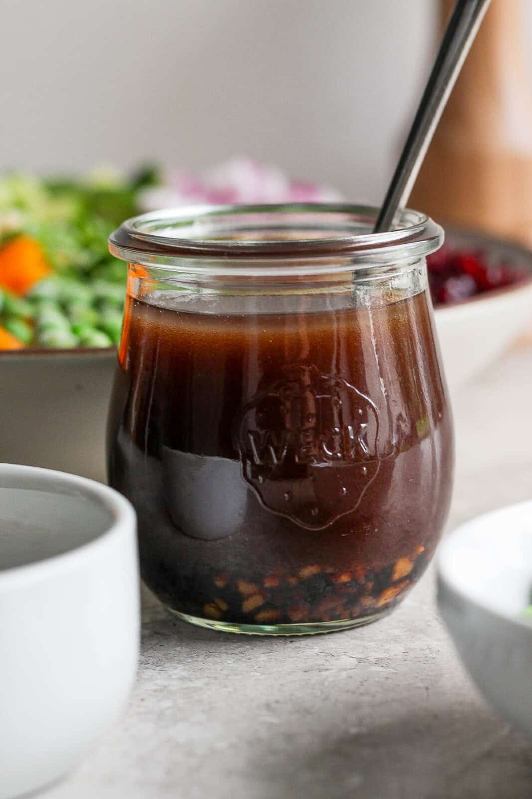 Balsamic vinaigrette in a jar with a spoon sticking out the side for summer quinoa salad bowls.