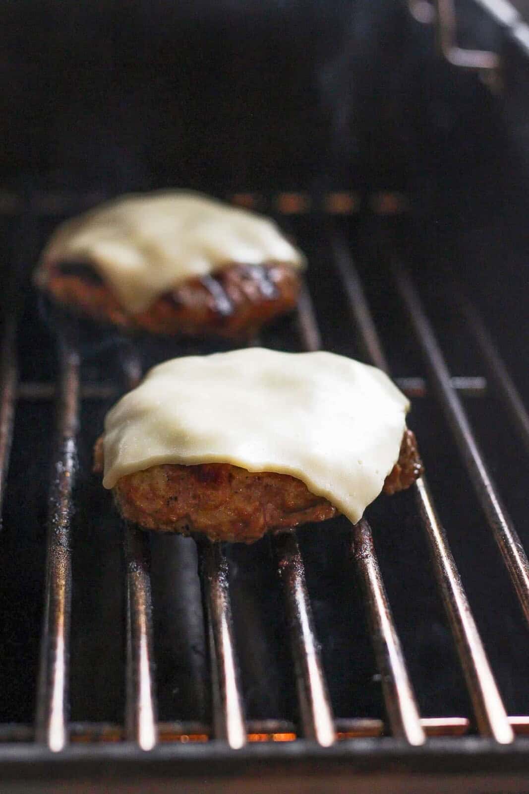 Avocado turkey burgers cooking on the grill with slices of cheese on them.