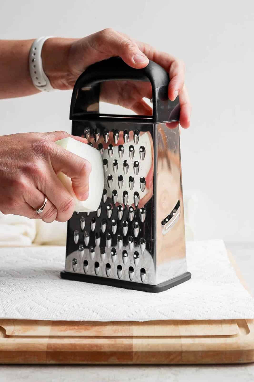 A quarter of a white onion being grated to add to avocado turkey burgers.