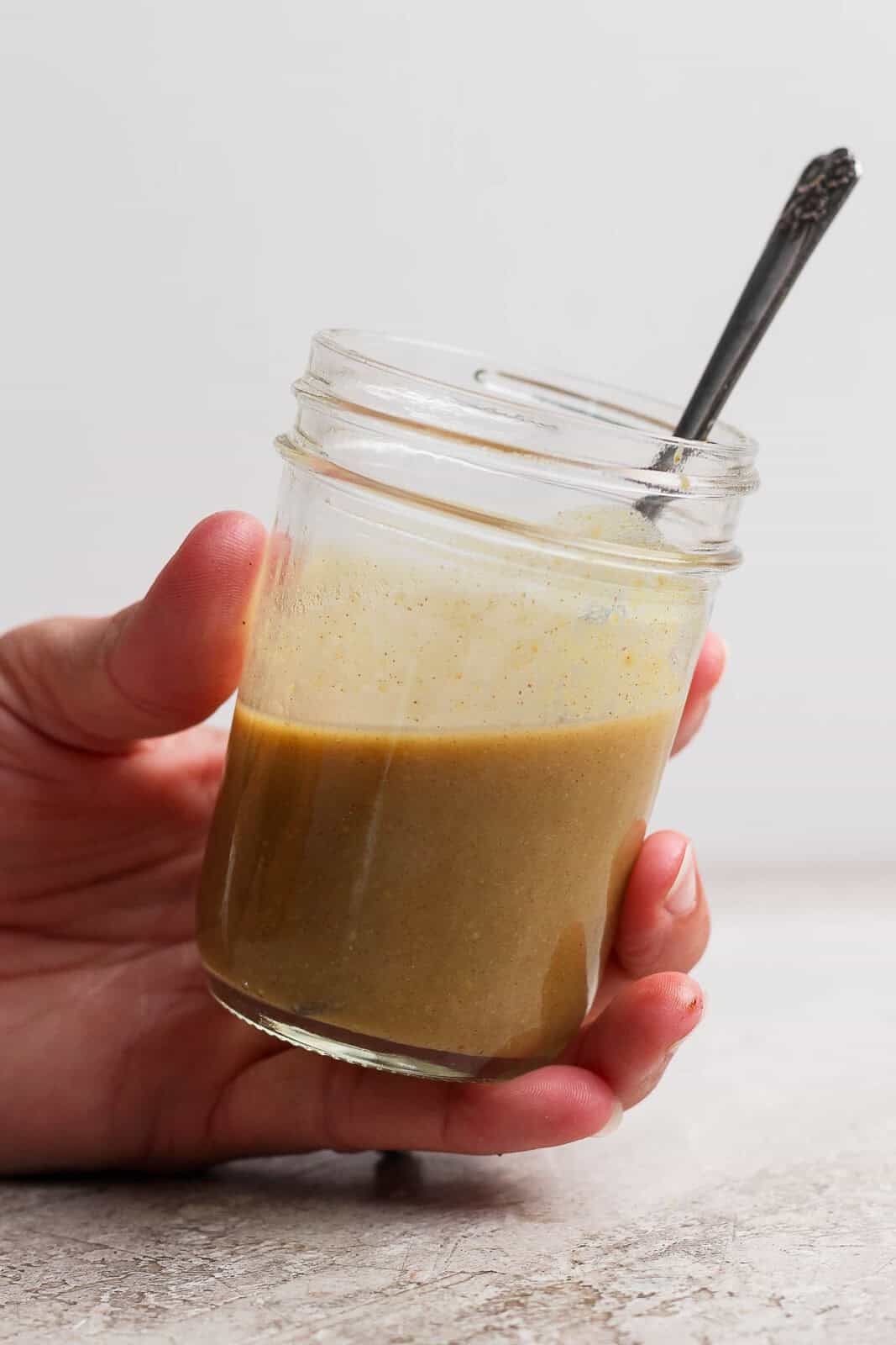 Someone holding a mason jar of maple dijon dressing with a spoon sticking out the top.
